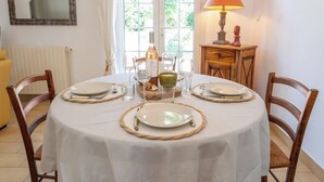 A dining table set for four with plates, cutlery, and glasses, a wine bottle, and a lamp on a wooden side table. - Les Sablettes Jardin & Parking 5 min de la Plage (La Seyne-sur-Mer)