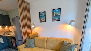 A living room with a sofa, a dining area with a kitchen, and two wall-mounted lamps. - Joli studio • 5 min plages • Tout à pied (Saint-Mandrier-sur-Mer)