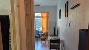 A hallway leading to a dining area with a table and chairs, a television, and a window with curtains. - Joli studio • 5 min plages • Tout à pied (Saint-Mandrier-sur-Mer)