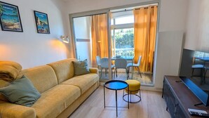 A living room with a sofa, a small round table, a TV, and a window with curtains. - Joli studio • 5 min plages • Tout à pied (Saint-Mandrier-sur-Mer)