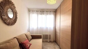 A modern living room with a sofa, a mirror, a hanging light fixture, and a sliding door closet. - Joli T3 spacieux & climatisé – confort + wifi (Toulon)