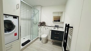 Ein kleines Badezimmer mit Duschkabine, Toilette, Waschbecken mit Spiegel und einer Waschmaschine.