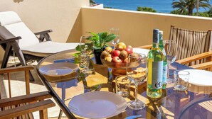 Ein Tisch mit Tellern, Gläsern, einer Flasche und Früchten auf einem Balkon mit Blick aufs Meer.