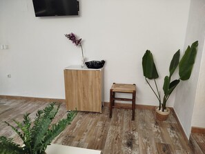 Une pièce avec un meuble en bois, un petit tabouret, une plante en pot et un téléviseur fixé au mur.