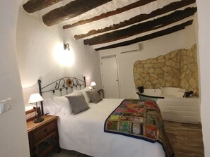 Quarto com cama, mesa de cabeceira, luminária, parede de pedra e banheiro com banheira.