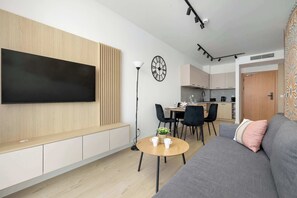 Un soggiorno moderno con TV a schermo piatto, un tavolino rotondo, un divano e un'area pranzo con sedie, con una cucina sullo sfondo.