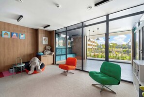 Een moderne kamer met grote ramen, een groene stoel, een oranje stoel en een wit pluchen dier op een poef.