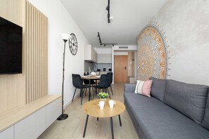 Een moderne woonkamer met een bank, een salontafel, een televisie bevestigd aan een houten paneel, een eethoek met stoelen en een tafel, en een keuken op de achtergrond.