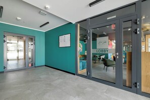 Una hall con pareti color acquamarina, un ingresso con porta in vetro e un'area salotto con un cartello che riporta la scritta 'Lobby'.