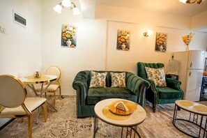 A living room with a green sofa, a dining table with chairs, and artwork on the walls. - Vaasi place Furnished 1 bedroom  apartment with an extra mini bed (Nairobi)