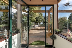 Una puerta de cristal da a un patio con césped, plantas en macetas y mobiliario de exterior.