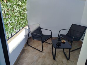 Un petit espace extérieur aménagé avec deux chaises et une table, une lanterne et un mur recouvert de feuillage verdoyant.