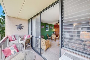 Ein Balkon mit Korbmöbeln, einer Schiebeglastür, einer grünen Wand und einem Deckenventilator.