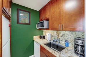 Una cocina con paredes verdes, armarios de madera, encimera de granito, microondas integrado, tostadora, cafetera y un fregadero.