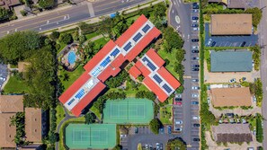 Vista aérea de un edificio con techo rojo, varios estacionamientos y canchas de tenis verdes.