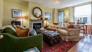 Una sala de estar con chimenea, un sofá verde, un sillón color beige y un tapiz rojo con estampado.