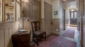Un pasillo con una silla de madera, un escritorio con libros, un espejo y una puerta.