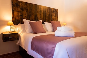 Una cama bien tendida con ropa de cama blanca y marrón, un cabecero de madera y dos lámparas de noche.