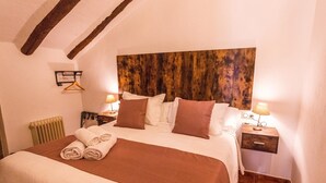 Un dormitorio con cabecera de madera, cama con ropa de cama blanca y marrón, dos mesitas de noche con lámparas y un radiador.