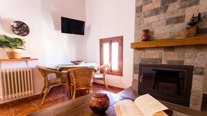 Una sala de estar acogedora con chimenea, televisor montado en la pared y comedor con sillas de mimbre y una mesa.
