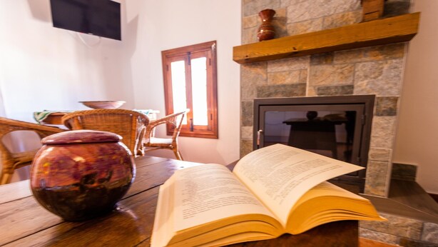 Un libro abierto sobre una mesa de madera, un jarrón y una chimenea.