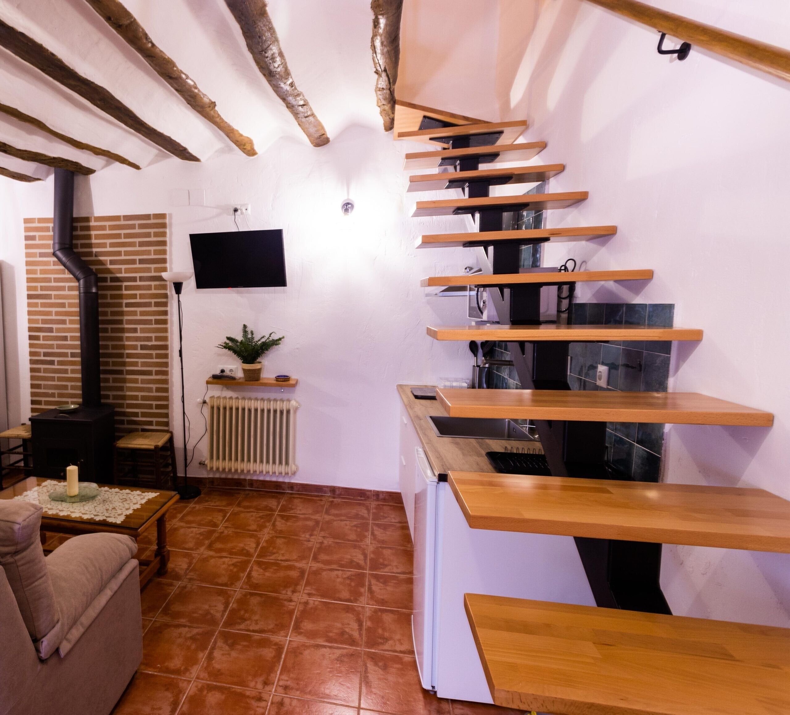 A modern interior with a wooden staircase, a fireplace, a television, and a dining area.
