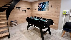 Een kamer met een tafelvoetbaltafel, houten wanden, een trap en een schilderij.