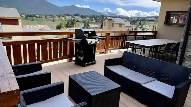 Een balkon met buitenmeubilair, een barbecue en uitzicht op een berg.
