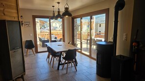 A dining area with a wooden table and chairs, a kitchen with a black trash bin, and a view of a patio with outdoor furniture.