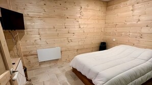 Een slaapkamer met een houten wand, een bed, een aan de muur bevestigde televisie en een betegelde vloer.