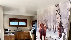 Een ruime keuken met houten kastjes, een groot raam en een schilderij van een stier in een besneeuwd bos.