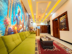 Un hall de hotel con un sofá verde, una recepción, un mural y una alfombra estampada.