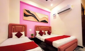 A hotel room with two beds, a pink accent wall, a modern abstract painting, an air conditioning unit, and a small potted plant. - Radha Palace (Vrindavan)