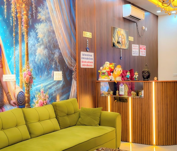Uma área de recepção com um sofá verde, um mural na parede, um aviso de proibido fumar e uma estátua de Buda.