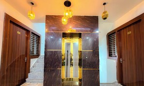 A hotel entrance with a marble wall, wooden doors, and a staircase leading to an elevator. - Radha Palace (Vrindavan)