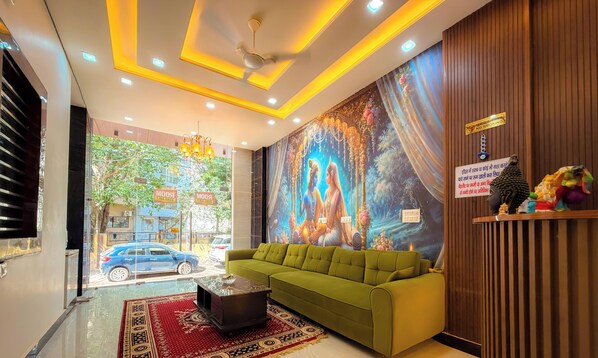 A hotel lobby with a green sofa, a chandelier, a mural, and a 'No Smoking' sign. - Radha Palace (Vrindavan)