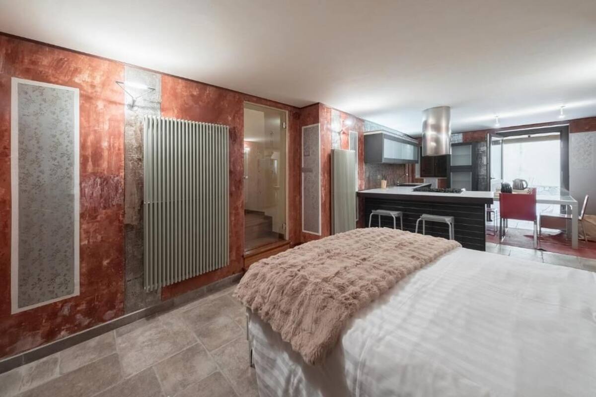 Ein modernes Schlafzimmer mit einem großen Bett, einer Küchenzeile inklusive Herd und Schränken sowie einem Badezimmer mit Dusche.