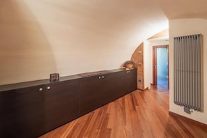 Een gang met een donker houten kast, een radiator en een deur naar een andere kamer.