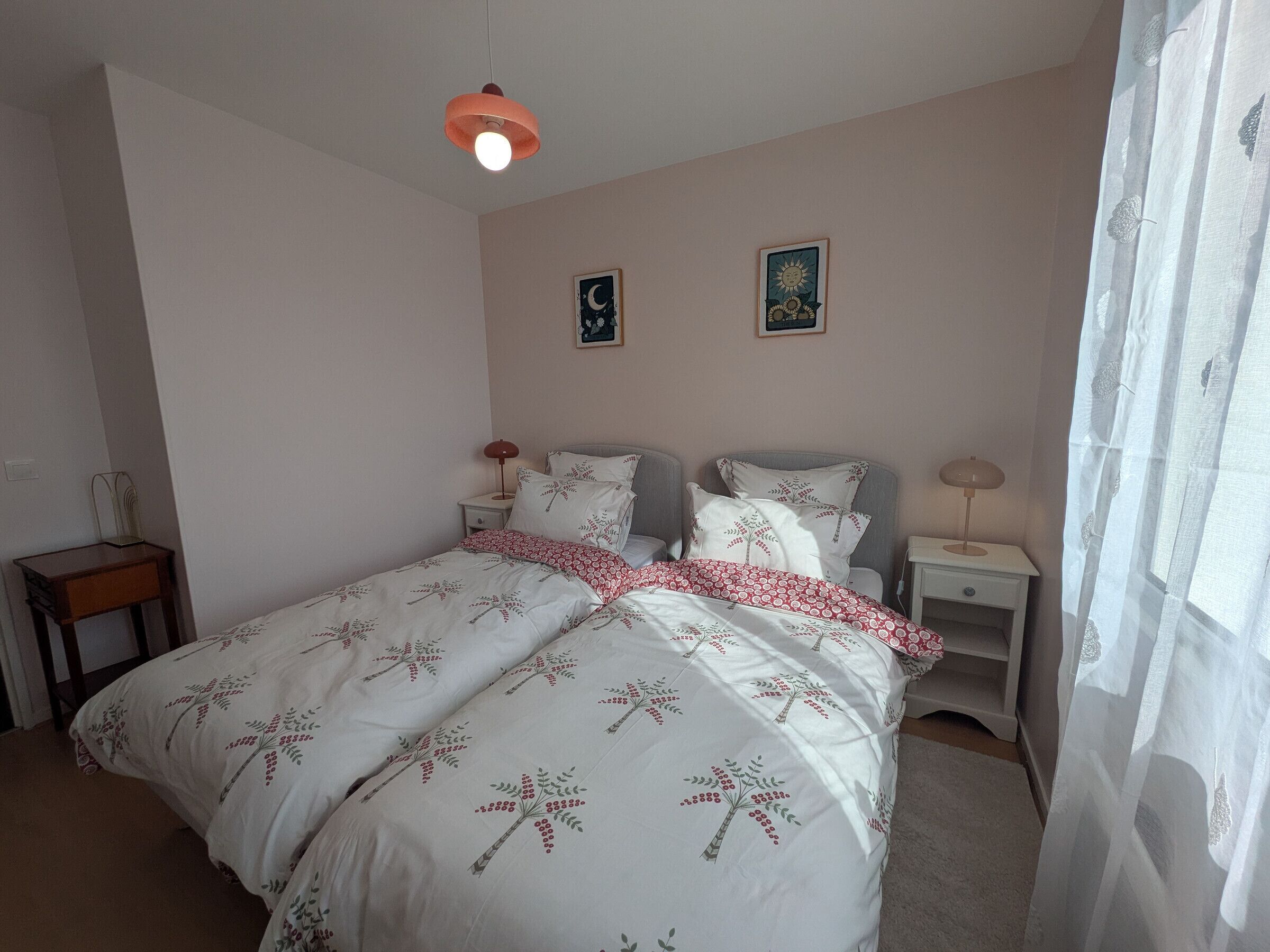 Un dormitorio con cama, dos mesitas de noche, lámpara colgante y dos cuadros en la pared.