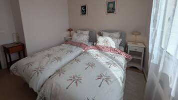 Un dormitorio con cama, dos mesitas de noche, lámpara colgante y dos cuadros en la pared.