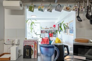 Une cuisine équipée d’une machine à café, d’une bouilloire et de tasses suspendues.