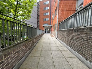 Une ruelle étroite, avec un bâtiment en briques d’un côté et une clôture en métal de l’autre.