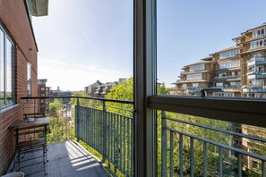 A balcony with a metal railing, a wooden table, and a view of surrounding buildings and greenery. - Cosy Canalside Retreat in the Heart of West London (London)