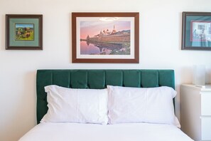 Ein Hotelzimmer mit einem grünen, bezogenen Kopfteil, weißer Bettwäsche und drei gerahmten Bildern an der Wand.