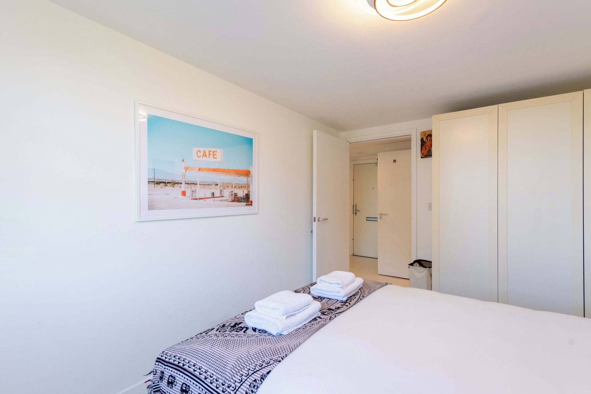 A hotel room with a bed, a framed picture of a cafe, a door, and a wardrobe.