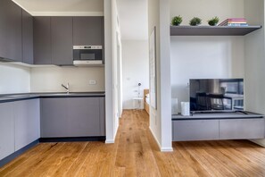 A modern kitchen with grey cabinets, a wooden floor, a built-in microwave, and a small white table in the background. - w Bright 1BR Near to the Center of Milan (Milan)