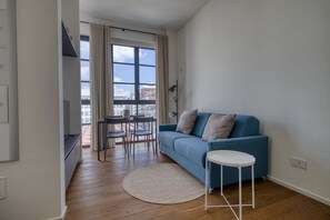 A modern living room with a blue sofa, a small round table, a dining area with chairs, and a large window with curtains. - w Bright 1BR Near to the Center of Milan (Milan)