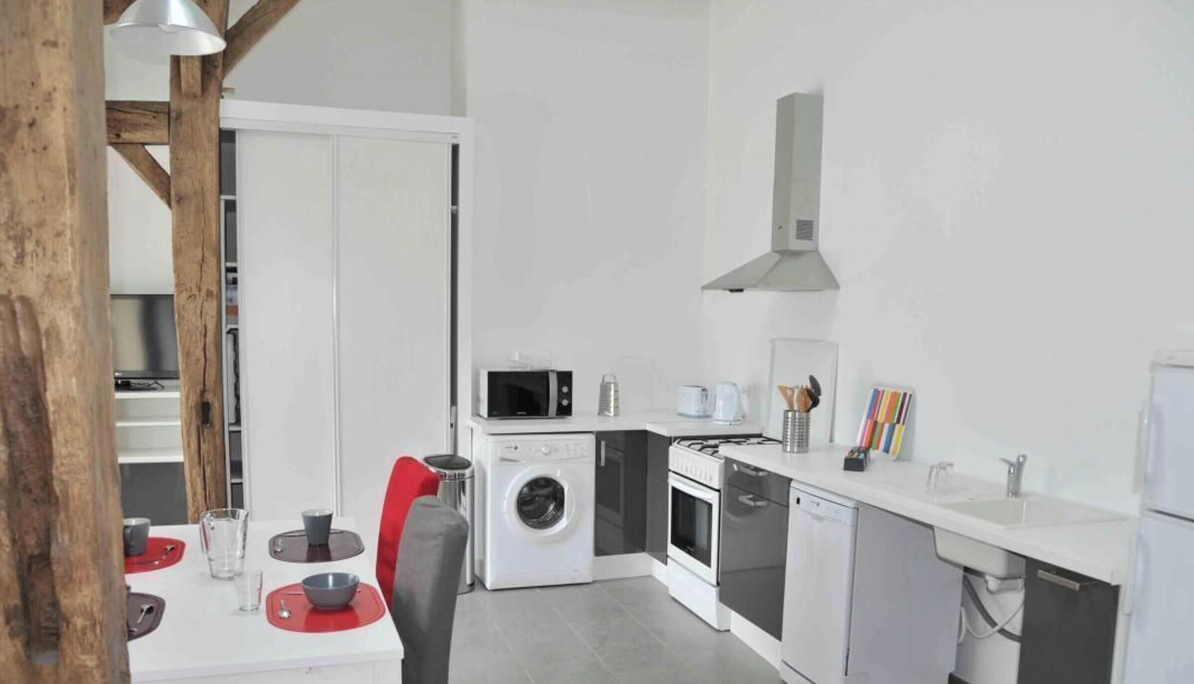 Una cocina moderna con microondas, horno, lavadora y un comedor con mesa y sillas.