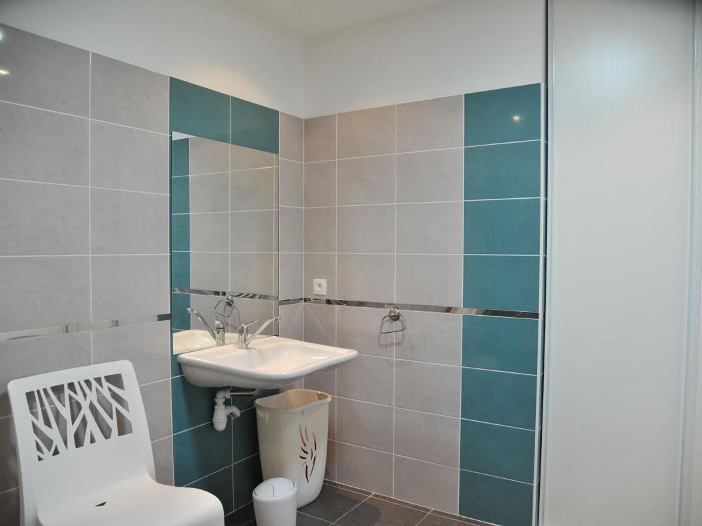 A bathroom with a white sink, a mirror, and a white chair.