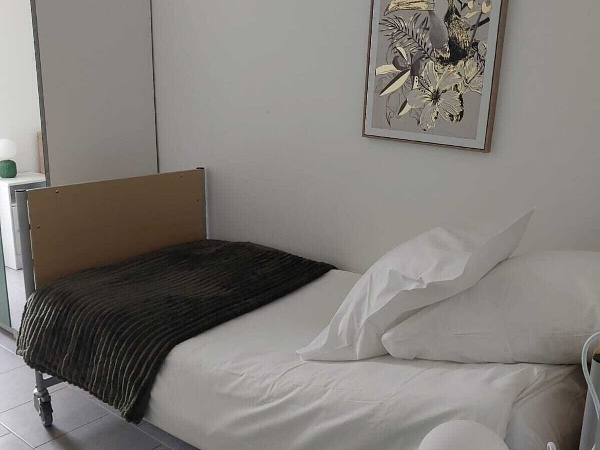 A single bed with a wooden headboard, white bedding, and a framed floral artwork on the wall.